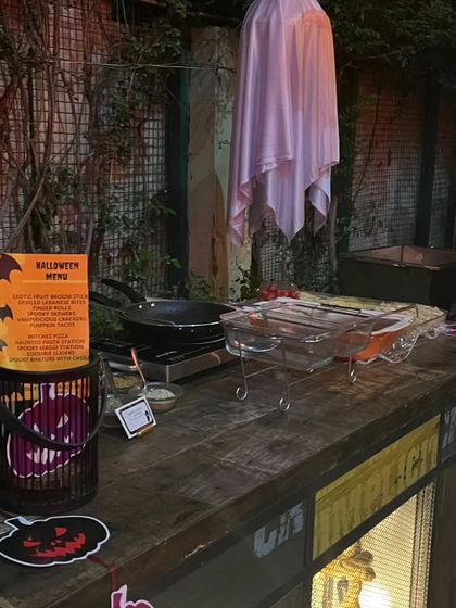 Another view of the Halloween food station, complete with a hanging ghost, a jack-o'-lantern bucket, and a themed menu, ready for the chef to start cooking.