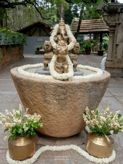 A Ganesha idol placed in a large stone urn, decorated with simple white flower garlands for an elegant touch.