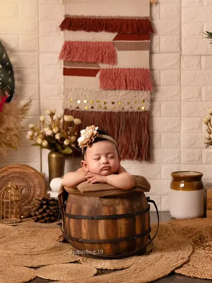 This little one looks so serene posing in a rustic wooden bucket as part of our popular boho-themed newborn shoot. We use natural textures like jute, wood, and macrame to create a warm, earthy, and timeless look.