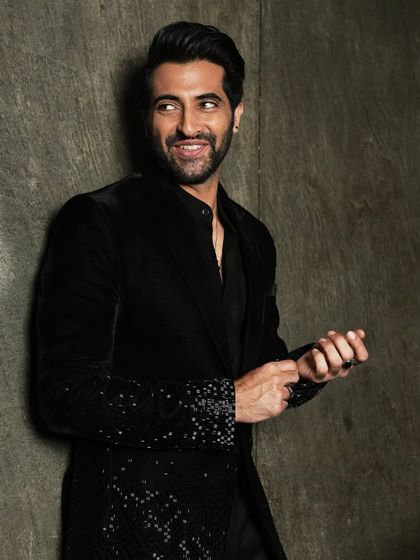 A standing portrait of Akshay Oberoi against a textured wall, offering a different look within the same location.