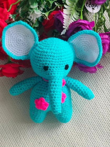 A single crochet elephant toy, sitting in front of some flowers. A very pretty gift for an animal lover.