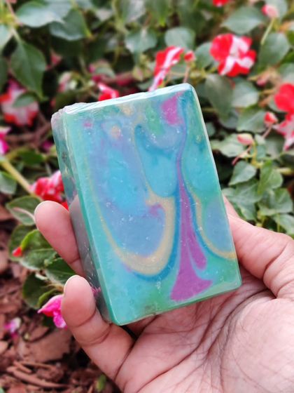 A beautiful cold process soap with swirls of teal, magenta, and gold. Holding it in my hand against a backdrop of flowers reminds me that nature is my biggest inspiration.
