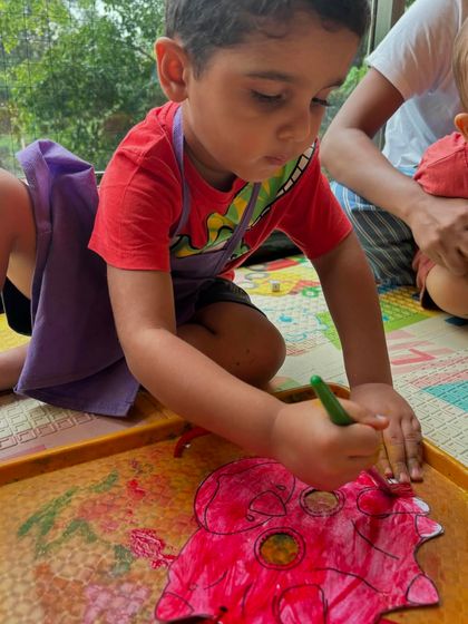 A young paleontologist coloring a dinosaur cutout. We use a mix of painting, coloring, and sensory play to explore our weekly themes from every angle.