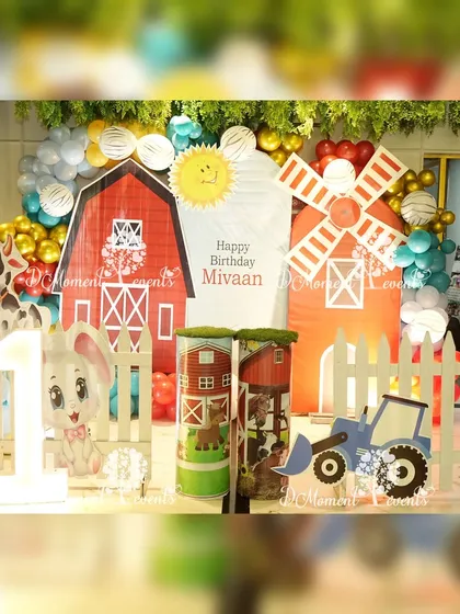 A charming farmland-themed stage featuring red barn cutouts, a windmill, and cute farm animal props for a rustic and fun first birthday.