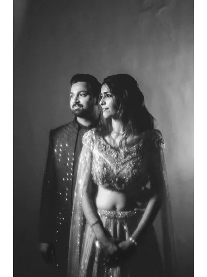 A timeless black and white studio portrait. The classic lighting creates soft shadows and highlights, focusing on the couple's elegant pose and the texture of their outfits.