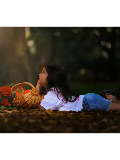A dreamy, cinematic shot of a young girl lying in the autumn leaves, gazing at the light. Outdoor sessions allow for artistic and creative portraits.