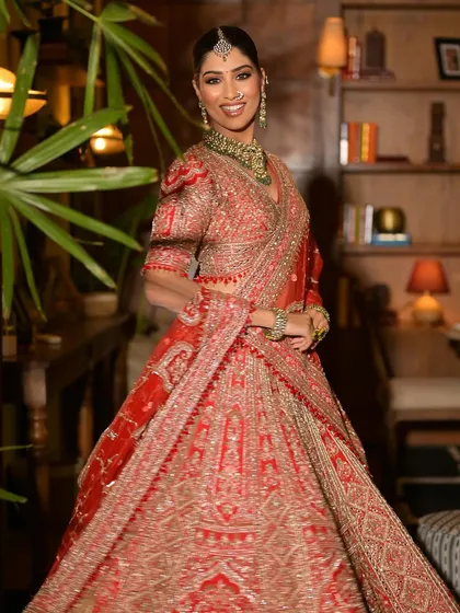 A full-length shot of a bride in a gorgeous red lehenga, adorned with a statement green necklace set. This showcases how my jewellery can elevate a traditional outfit.