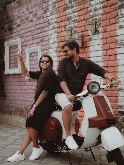A fun and energetic shot of the couple on a vintage scooter against a colorful brick wall.