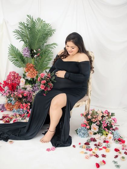 A beautiful seated portrait surrounded by a cascade of colorful flowers. The mom-to-be glows in a classic black off-the-shoulder gown, creating a look of pure elegance.