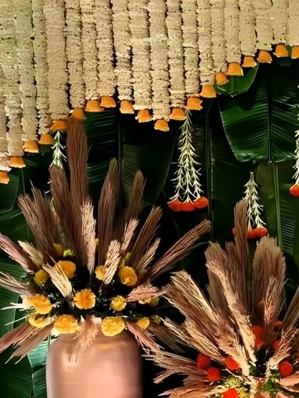 A close-up of a traditional decor element, featuring a backdrop of banana leaves, a curtain of white jasmine, and arrangements of dried grass and marigolds.