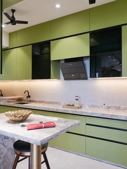 A wide-angle view showcasing the parallel counters of the sage green kitchen. The combination of matte green cabinets, black profile details, and a textured marble countertop creates a balanced and luxurious feel.
