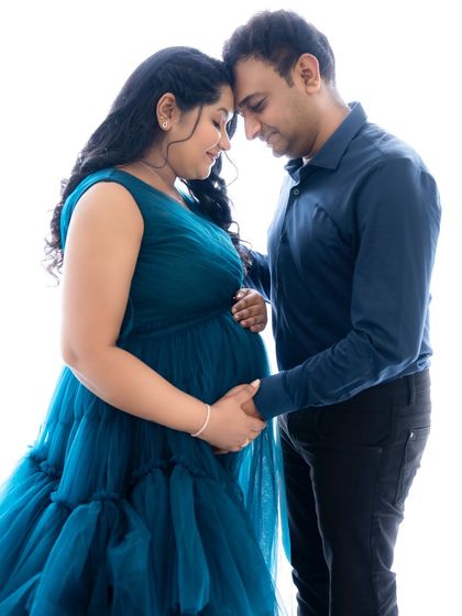 A close and intimate pose where the couple touches foreheads, their hands joined on the baby bump, dressed in coordinating blue outfits.