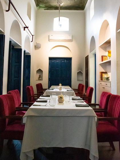 This long table setup is ideal for a family feast or a corporate lunch. The striking red chairs add a pop of color to the serene, white-walled room with its traditional Indian arches.