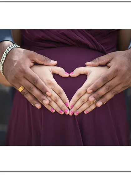 A beautiful close-up of the couple's hands making a heart shape on the bump, a classic symbol of love and family.