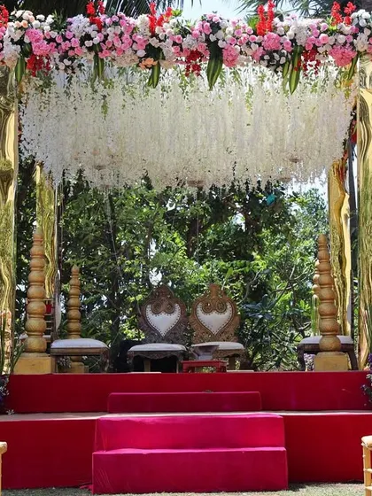 A close-up of a beautiful mandap with a cascading floral chandelier. The combination of white flowers and lush greenery against the gold structure creates a fresh and elegant look.