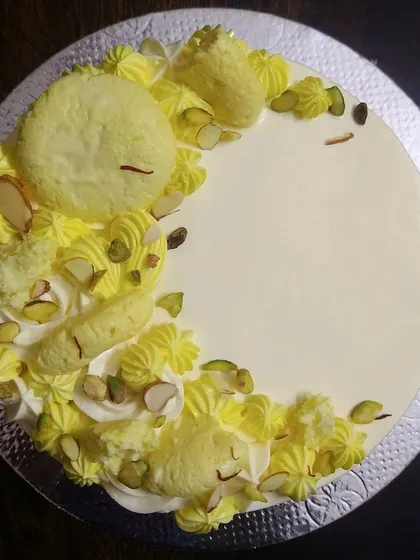 This is my popular Rasmalai fusion cake, seen from the top. It combines the soft texture of a vanilla sponge with the rich, creamy flavor of rasmalai, garnished with real rasmalai pieces, pistachios, and saffron.
