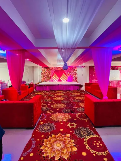 A full view of a banquet hall decorated for a wedding event. I arranged the guest seating with red sofas and created a beautiful stage with pink and white drapes.