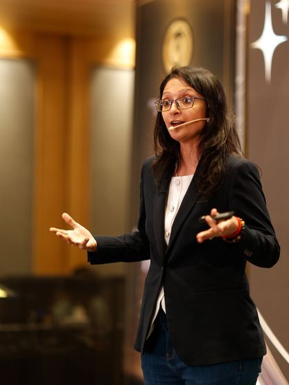 Speaking on stage in a black suit. Your job may end one day, but your book, your brand, and your impact live on. Your real promotion is becoming the author of your life.