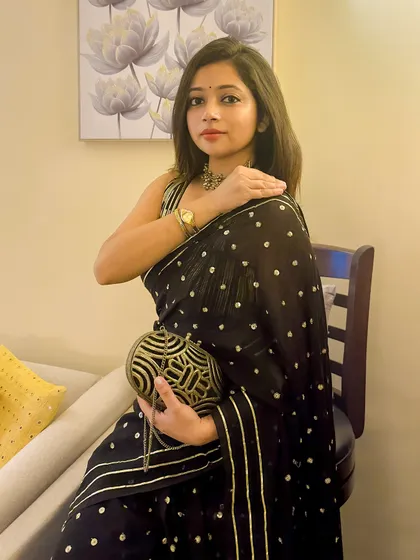 Holding the beautiful antique-finish clutch that complements the sequin work on the saree. A statement bag is a must-have for any wedding guest outfit.