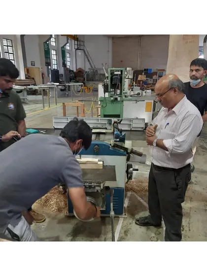 An instructor explains the mechanics of a mortising machine to a group of students and visiting officers from the naval dockyard. This machine is used to cut square or rectangular holes for mortise and tenon joints.