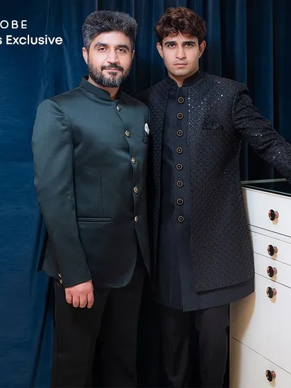 Two distinct yet complementary dark-toned outfits. One client wears a green Jodhpuri suit while the other is in a black textured Indo-western sherwani.