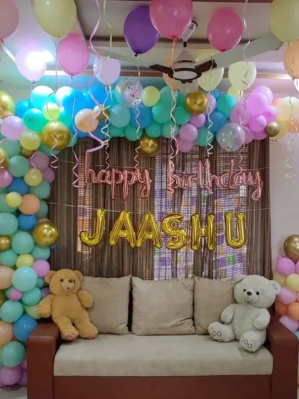 A pastel-colored balloon arch for a birthday party, complete with teddy bears. The soft, multi-colored balloons and rose gold foil letters create a sweet and gentle theme.