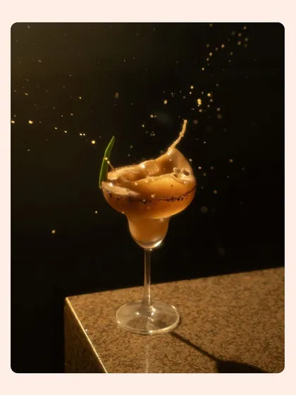 A dark and moody splash shot of a coffee-colored cocktail. The golden-hued droplets against the black background create a sense of luxury and excitement.