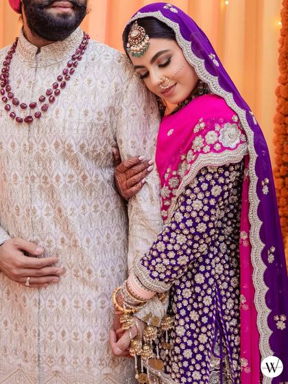 The bride and groom, with her elegant floral bun visible under the sheer purple dupatta.