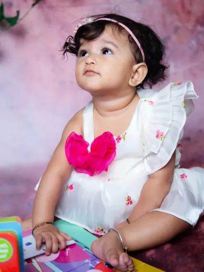 An adorable indoor studio portrait of a baby girl looking up with curiosity. Using a simple, colorful background and props can create a fun and engaging setting for baby photos.
