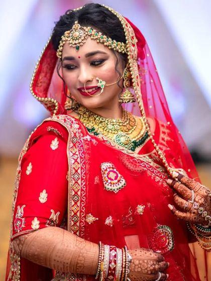 A stunning portrait of a bride in a red lehenga. Her look is completed with a heavy bridal set featuring a choker, layered necklace, and an elaborate matha patti.