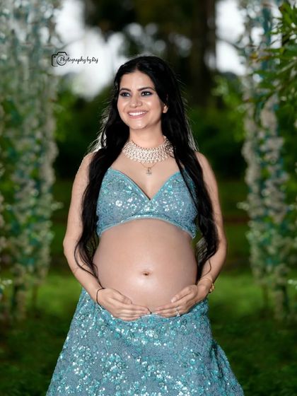A joyful bare-bump portrait in our outdoor setting. The mother-to-be is wearing a sparkling blue two-piece lehenga, celebrating her pregnancy with confidence and style.