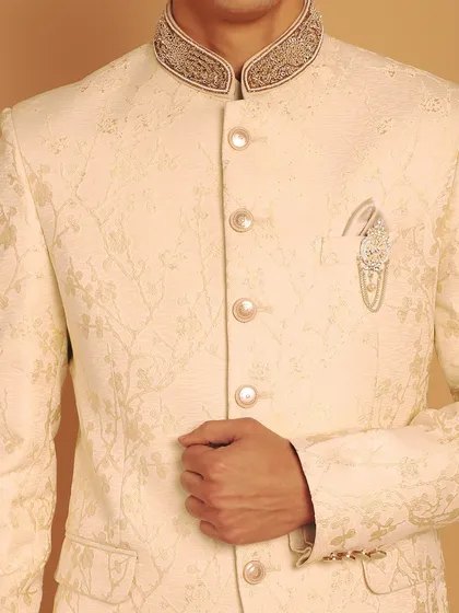 The beauty of this ivory Jodhpuri suit is in its details. Here, you can see the intricate zardozi work on the collar and the custom brooch, designed to make you feel like royalty.