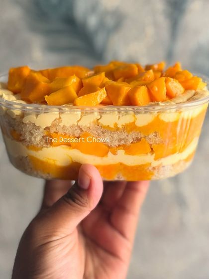 My Fresh Mango Cake Tub held up to show the beautiful layers. It features vanilla sponge, mango mousse, and lots of fresh mango chunks.