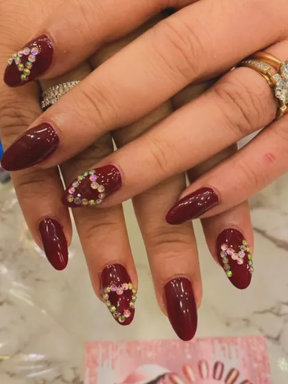 A romantic and glamorous choice, these deep red almond nails are perfect for a date night or party. The design features accent nails with heart shapes meticulously created from multi-colored rhinestones.