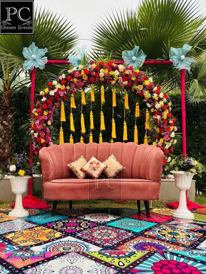 A bohemian-chic Mehndi setup in a garden. I used a vibrant printed carpet, a dusty rose sofa, and a floral arch with yellow tassels for a stylish and fun look.