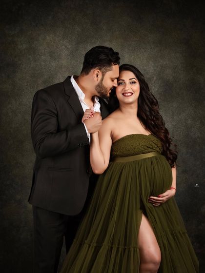 A classic and elegant couple portrait against a dark, moody backdrop. The client's olive green tulle gown and her partner's suit create a sophisticated and timeless look.