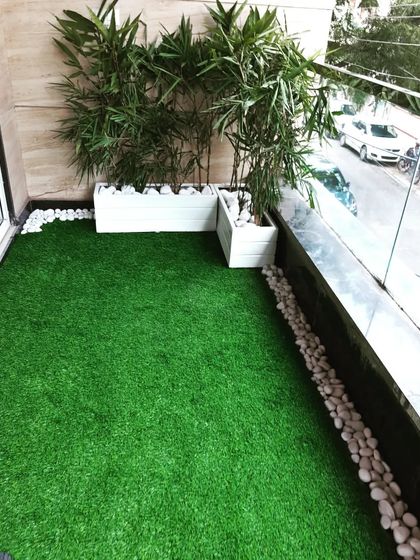 Another angle of the simple balcony makeover, showing how the artificial grass and pebbles create a neat border along the glass railing.