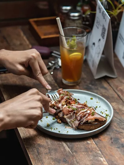 A customer enjoying one of our open-faced sandwiches, topped with cured meat and fresh greens, paired with a refreshing iced tea.