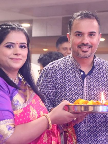 A couple participates in a traditional ceremony, holding a platter with a lit diya.