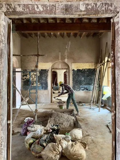 A view through a doorway into a room under full restoration. Piles of material and exposed ceiling joists show the messy, yet necessary, phase of deconstruction before the careful work of rebuilding can begin.