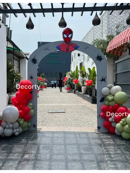 A Spider-Man themed entrance arch welcomes guests to the party. The arch is decorated with red, white, and green balloons and spider web details.