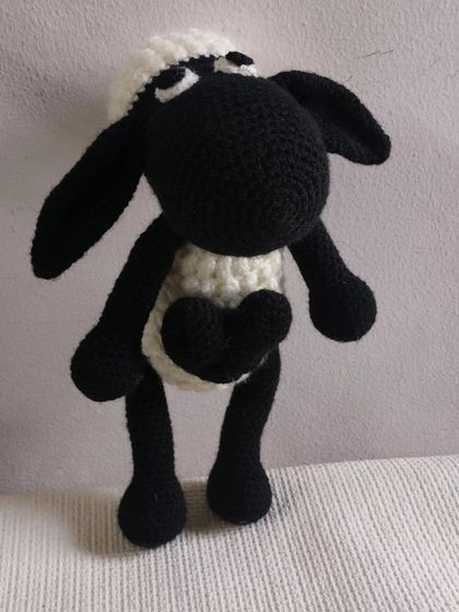 This crochet Shaun the Sheep is standing up. He has a little black heart on his chest.