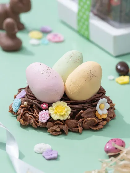 A chocolate nest made of crunchy flakes, holding three pastel-colored marzipan eggs. This is a playful and edible decoration, perfect for your Easter table.