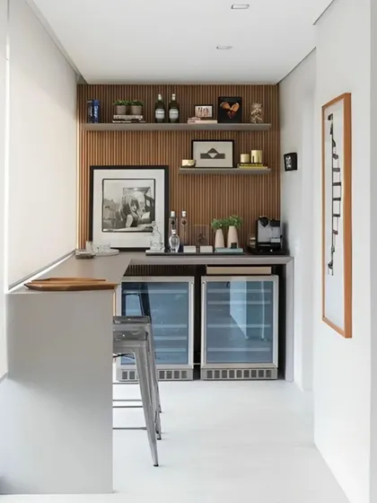 This sleek, modern bar is built into an enclosed balcony, creating a seamless indoor-outdoor entertainment space. It features two under-counter beverage coolers, open shelving against a wood-paneled wall, and a minimalist countertop with bar stools.