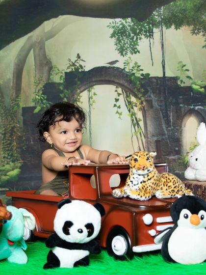 This older baby is ready for a jungle safari, sitting in a red truck with his animal friends.