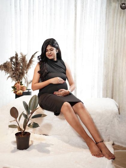 A full-length portrait in a simple black dress against a bright, clean background. The minimalist setup with a single plant prop adds a touch of modern style to the session.