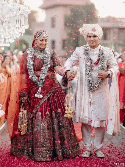 Rhea and Abhimanyu walking down the aisle hand-in-hand, showered with rose petals, their faces lit up with joy.