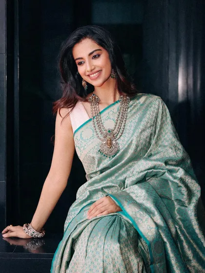 A seated portrait in the teal silk saree. The styling here feels intimate and graceful, highlighting the intricate jewelry and the soft smile of the model.