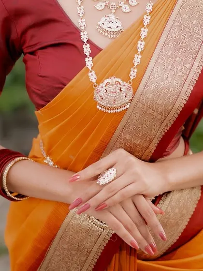 A detail shot focusing on the hands and jewelry of a model in a traditional saree. This highlights the intricate details of the accessories and the elegance of the pose.