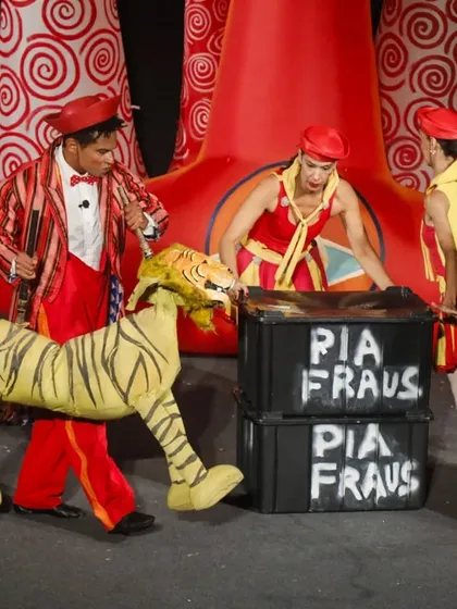 A performer dressed as a lion tamer leads a tiger puppet across the stage. The 'Air Giants Circus' shares the stage with a ferocious lion and tiger, all brought to life through puppetry.